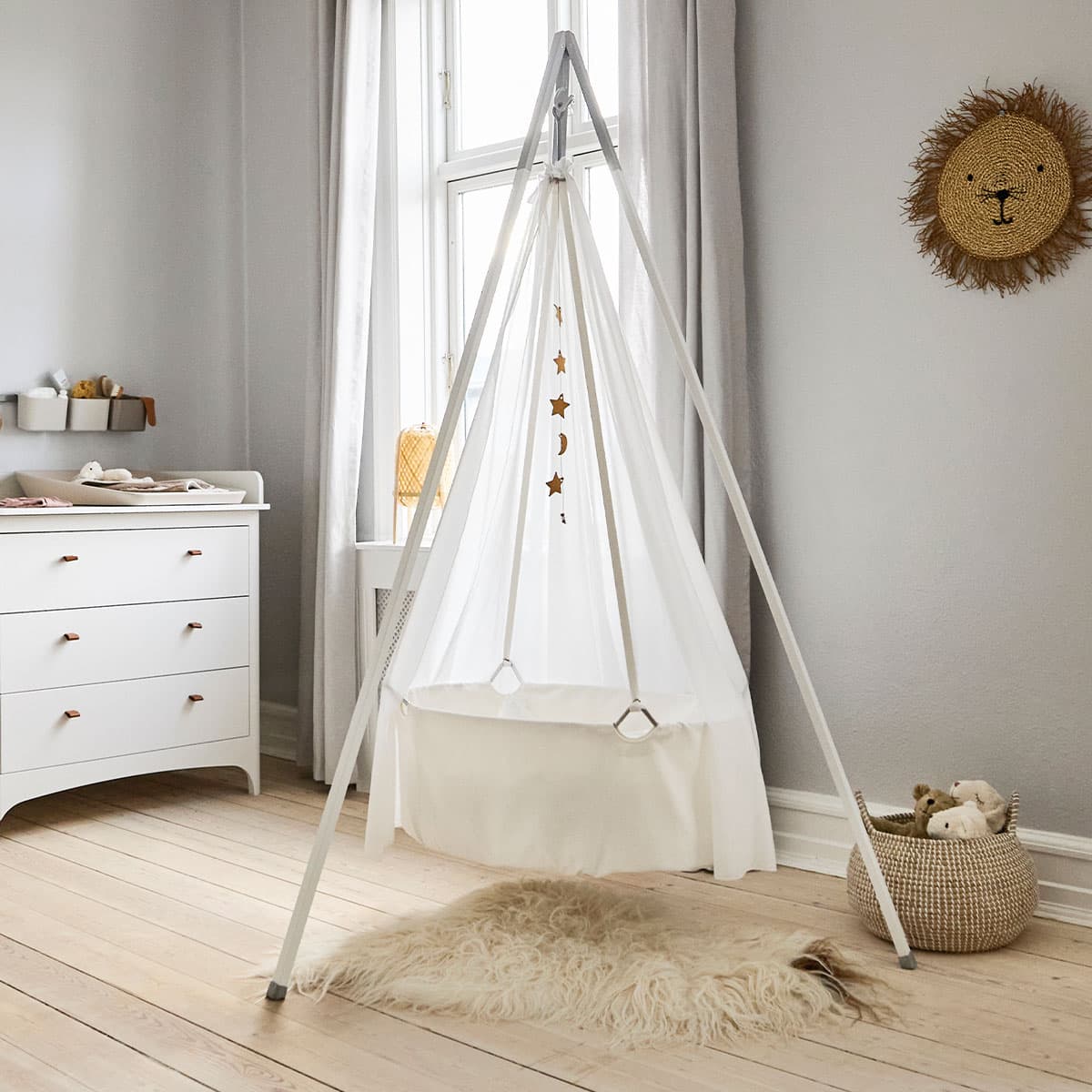 Leander Classic baby cradle in natural beechwood with white GOTS-certified cotton lining, suspended from a ceiling hook in a minimalist nursery
